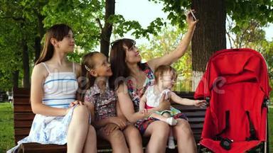 年轻的母亲在<strong>公园里坐在</strong>长凳上和孩子们打电话的时候被拍到了照片，并对小婴儿坐着微笑